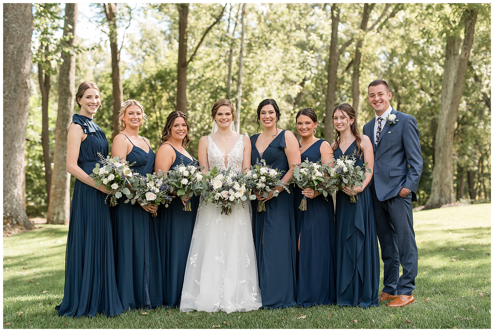 bride surrounded by her six bridesmaids in navy blue gowns and one bridesman man in navy blue suit at elizabeth furnace