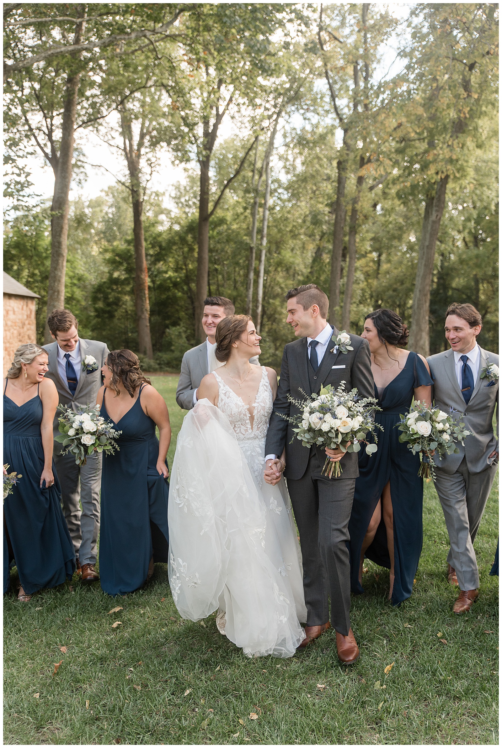 bride and groom walking in front of their bridal party and smiling at each other on sunny fall day in lancaster county