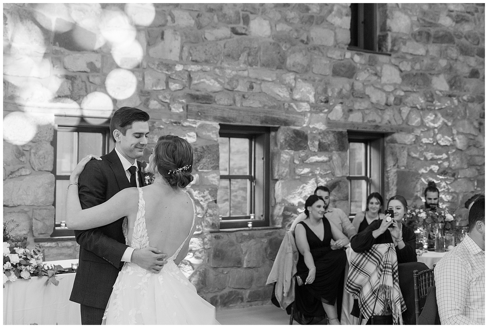 black and white photo of couple sharing their first dance inside stone barn as guests watch in lancaster county