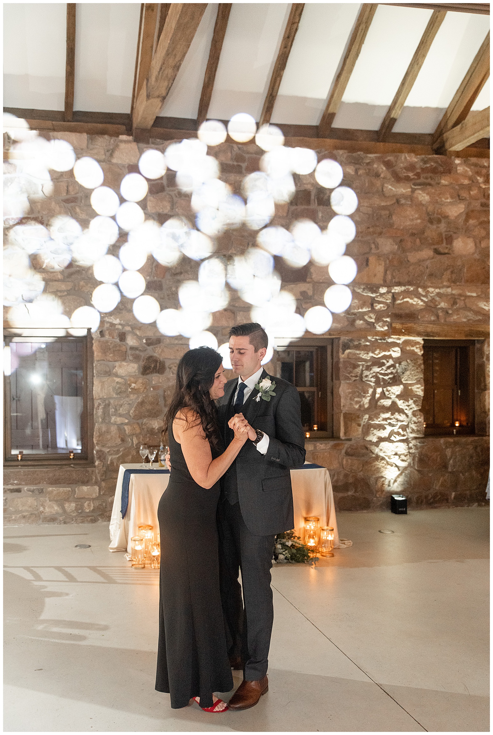 groom dancing with his mom who is wearing a long black dress inside stone barn at elizabeth furnace during reception