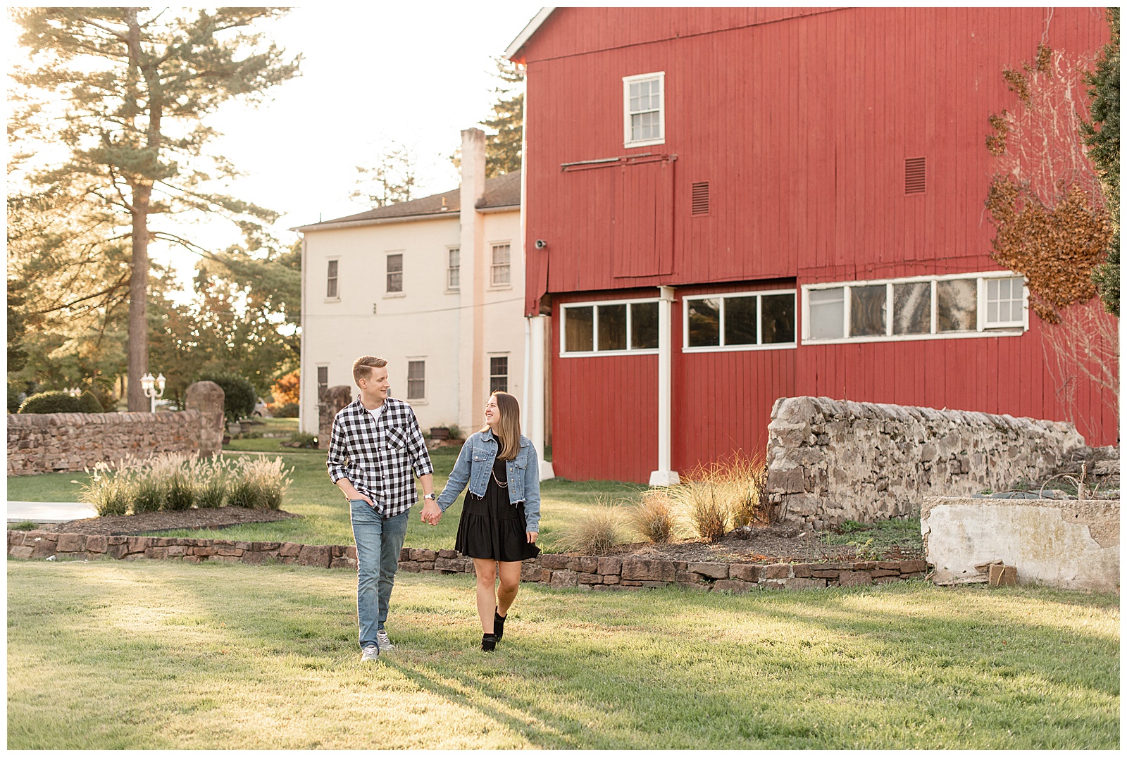 engaged couple holding hands and walking towards camera as they smile at each other by red barn in montgomery county pennsylvania