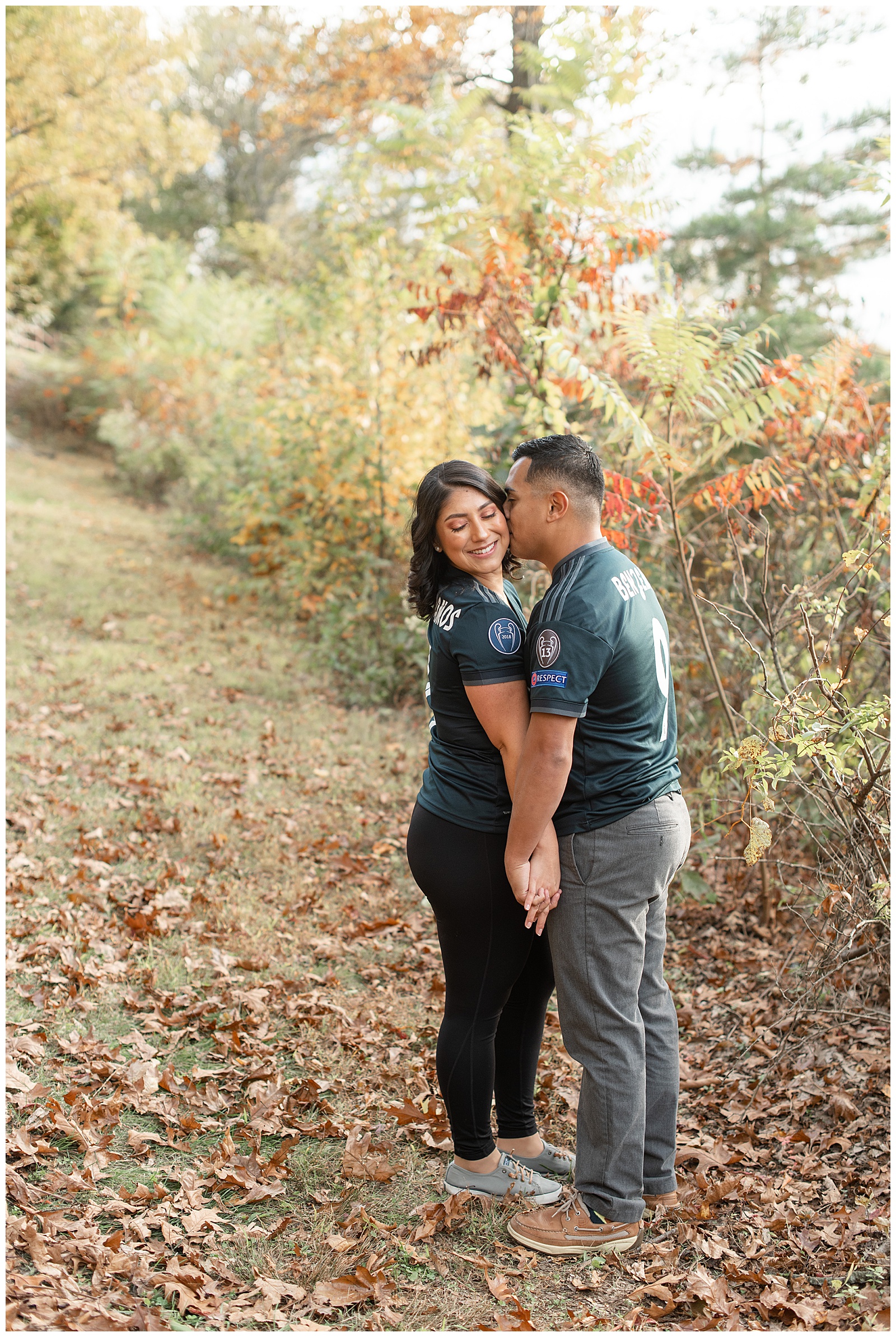 engaged couple wearing matching soccer jerseys standing close holding hands by colorful leaves at pinnacle point