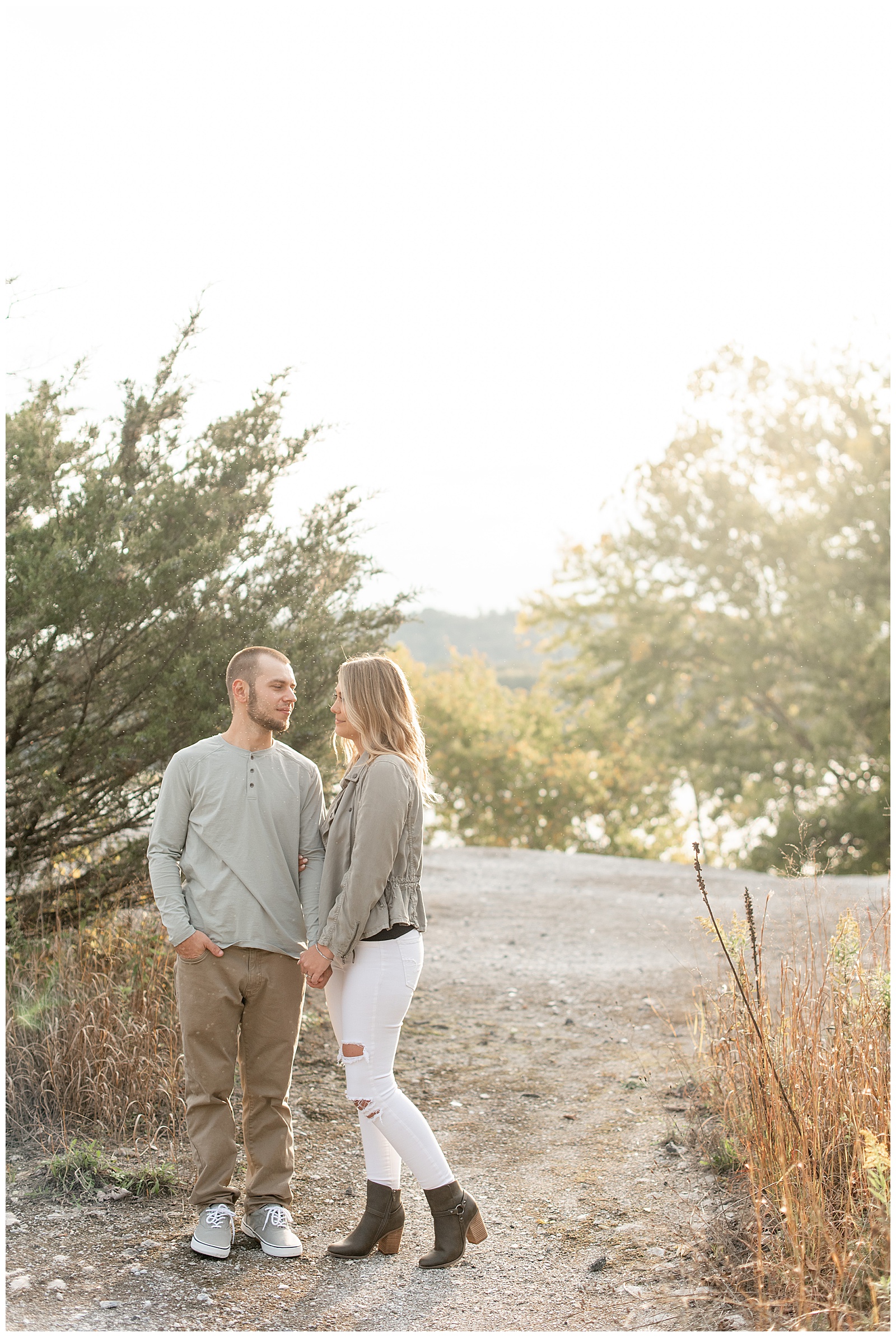 engaged couple holding hands and smiling at each other with sun setting behind trees behind them atop the white cliffs of conoy