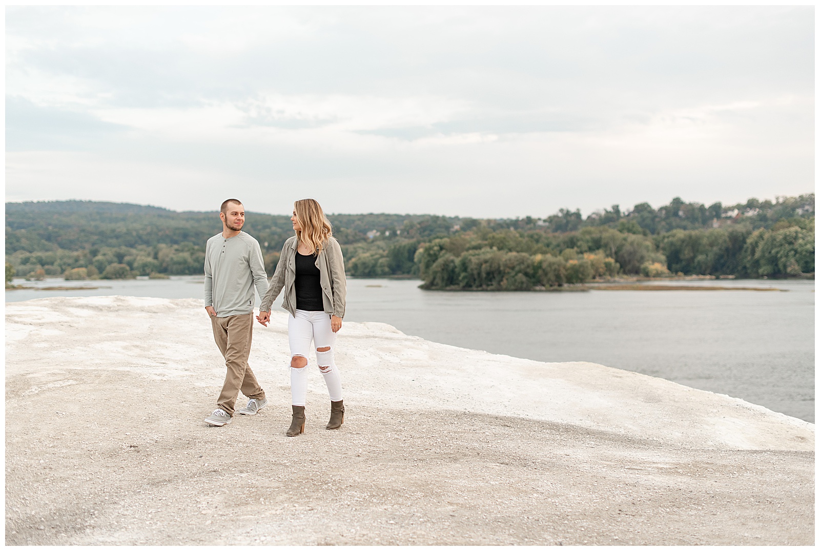 couple holding hands and walking along the white cliffs of conoy with susquehanna river and trees behind them
