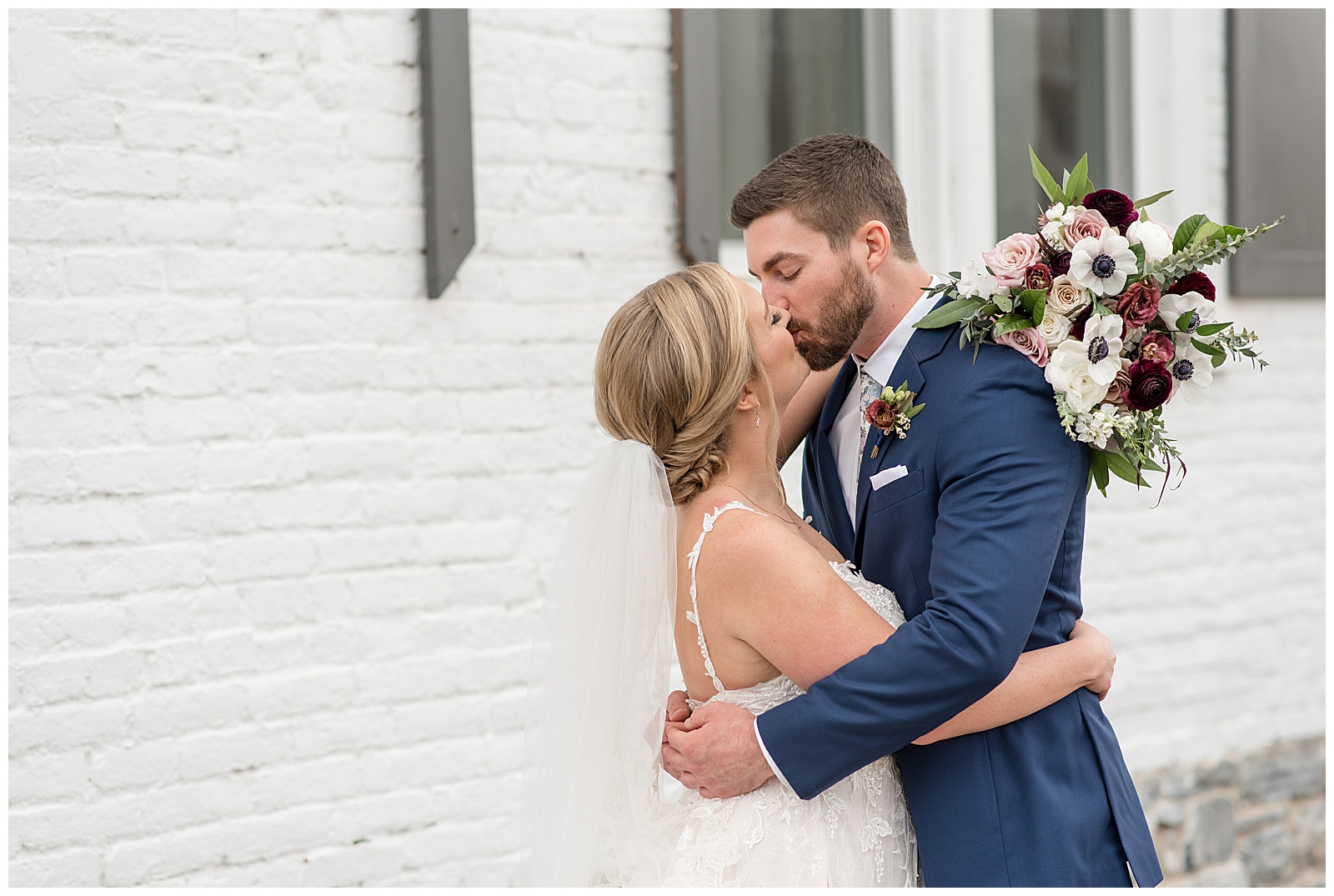 bride and groom share a kiss after first look moment by white brick building in wrightsville pennsylvania