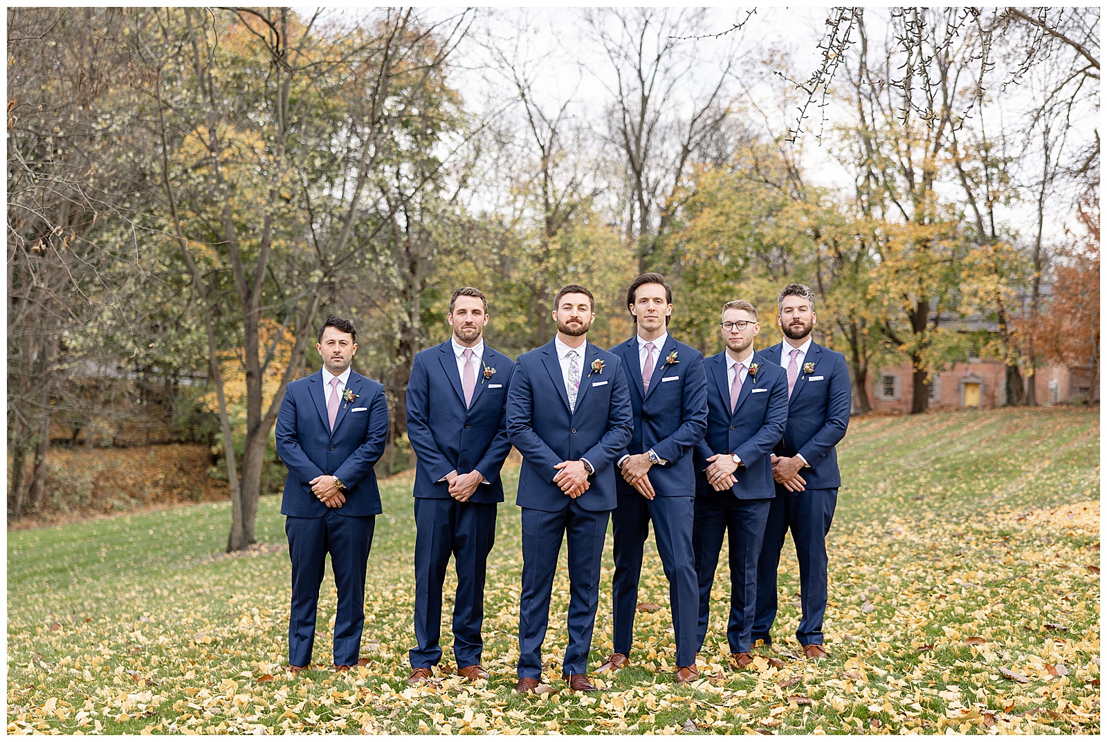 groom standing in a "v" with his five groomsmen all wearing navy blue suits with colorful fall leaves on trees at historic ashland