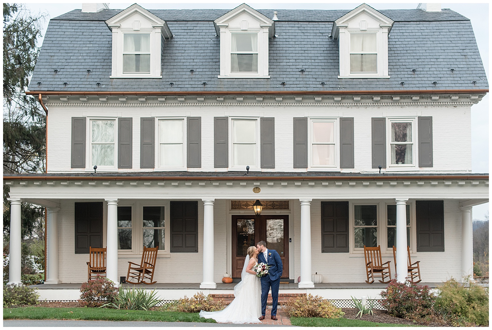bride and groom kiss in front of porch of white and gray farmhouse at historic ashland in wrightsville pennsylvania