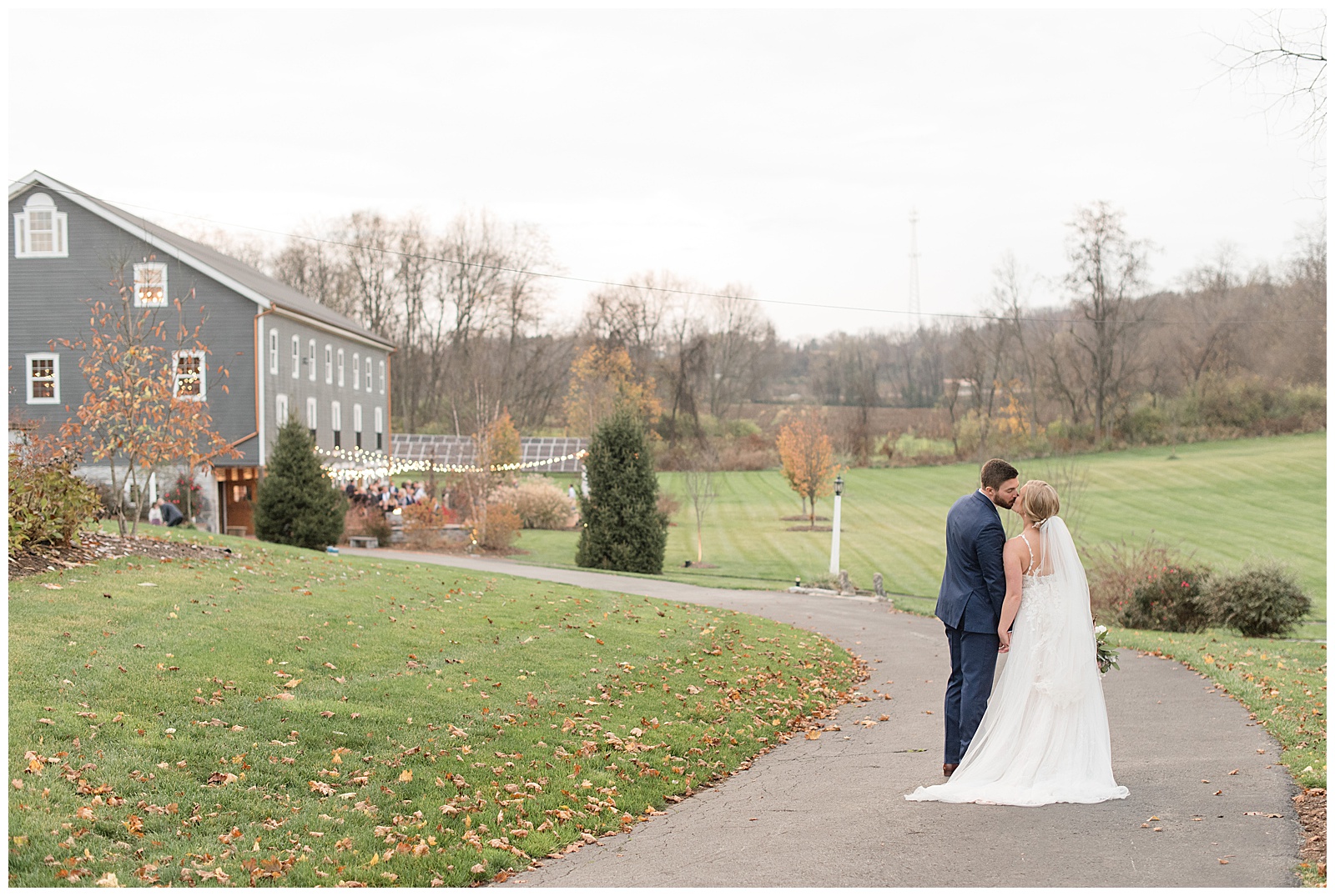 couple kissing while standing on paved path that leads to reception with their backs toward camera at historic ashland