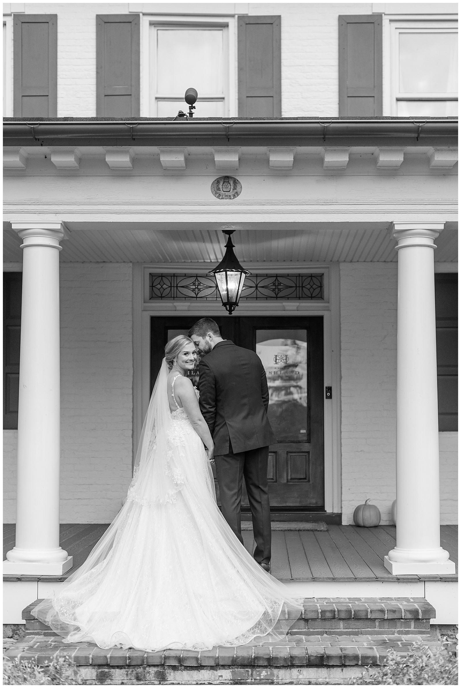 black and white photo of couple with backs toward camera as bride looks back on front porch at historic ashland