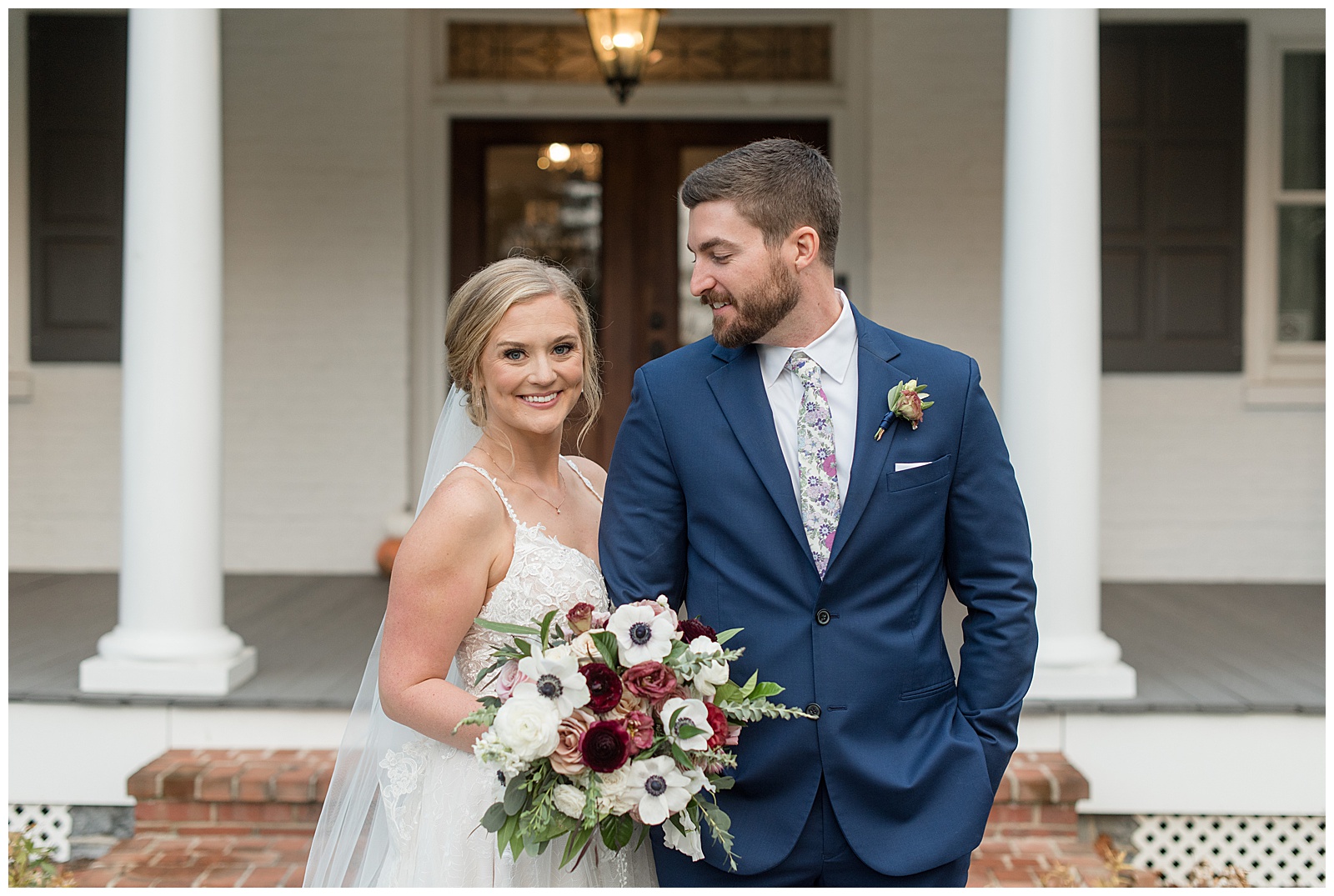 bride holding onto groom's right arm as he smiles and looks at her by farmhouse at historic ashland in pennsylvania