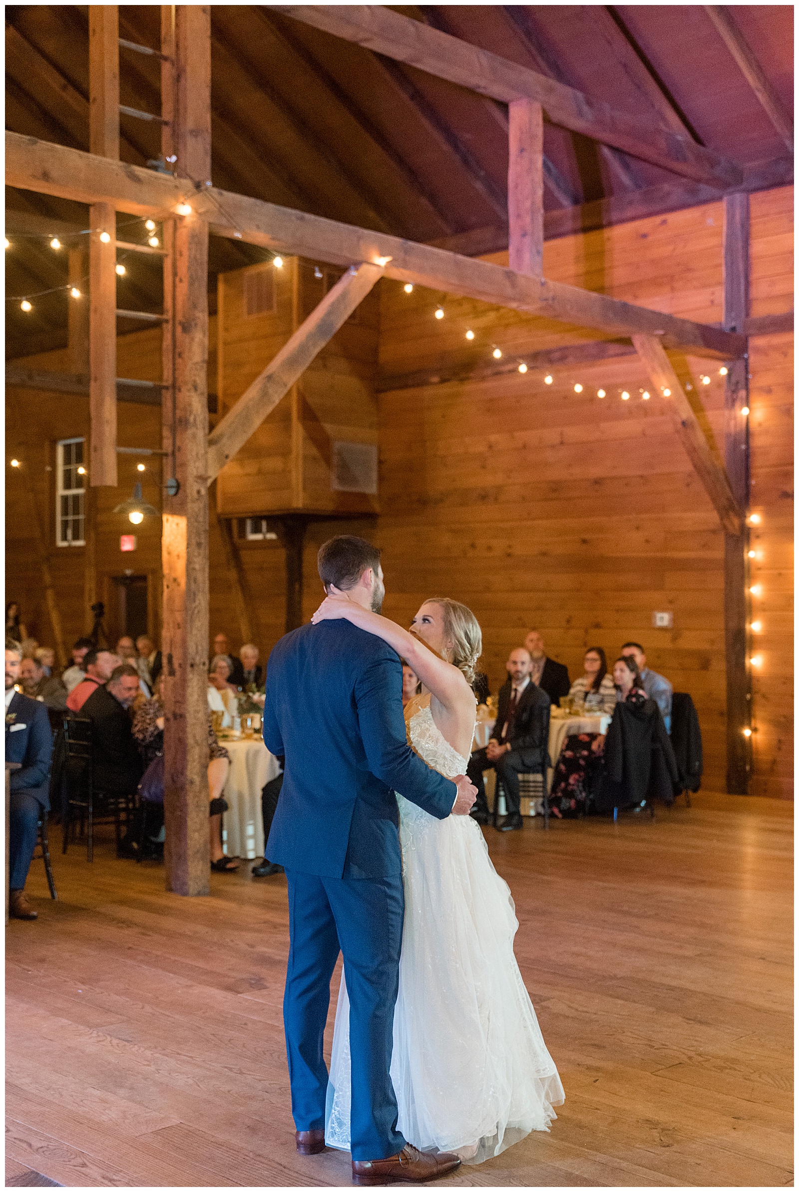 couple sharing their first dance as guests watch inside beautiful barn at historic ashland with glowing string lights