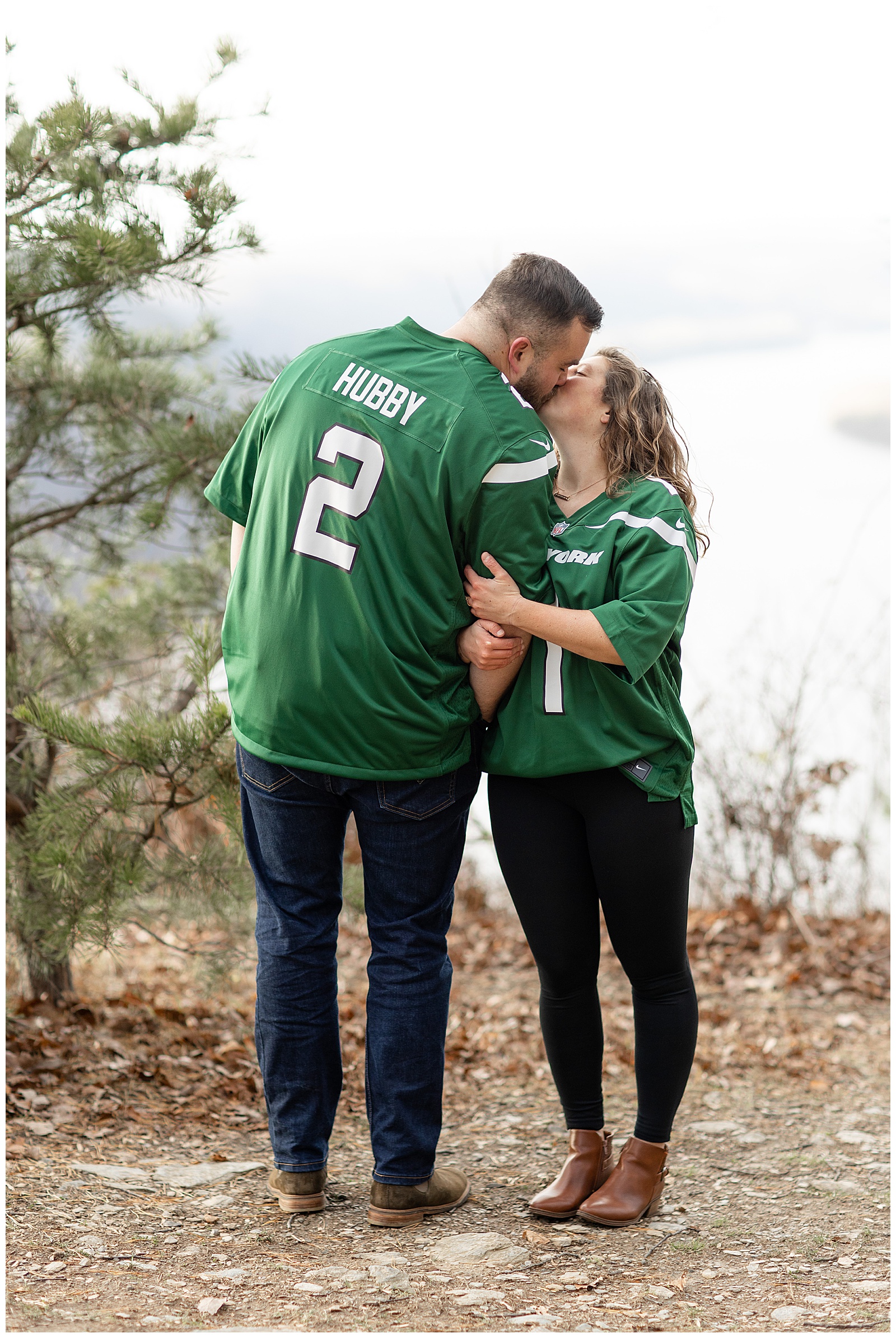 engaged couple wearing matching new york jets football jerseys and dark pants as they kiss at pinnacle overlook