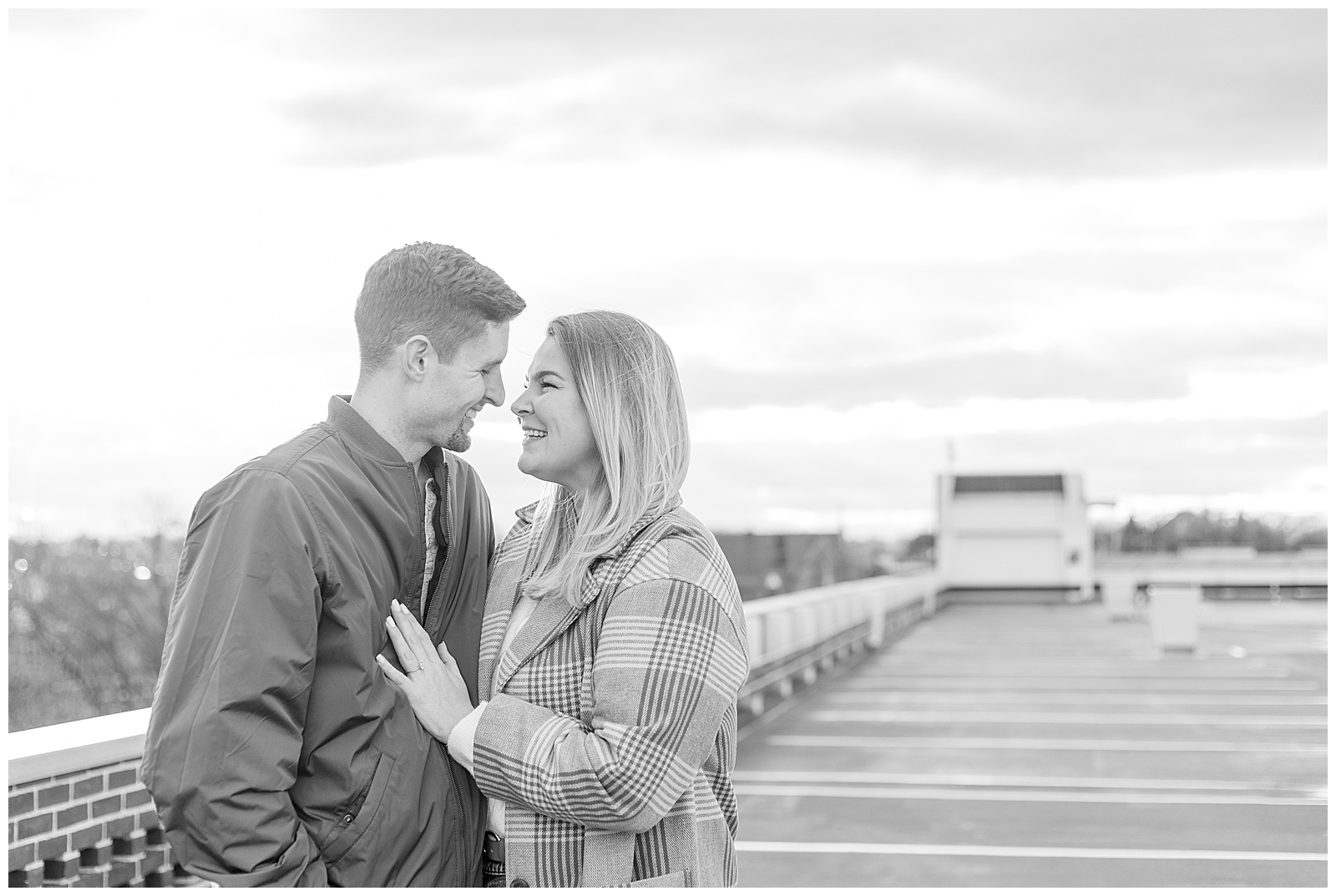 black and white photo of engaged couple standing close almost kissing on top level of parking garage on bright fall day in downtown lancaster
