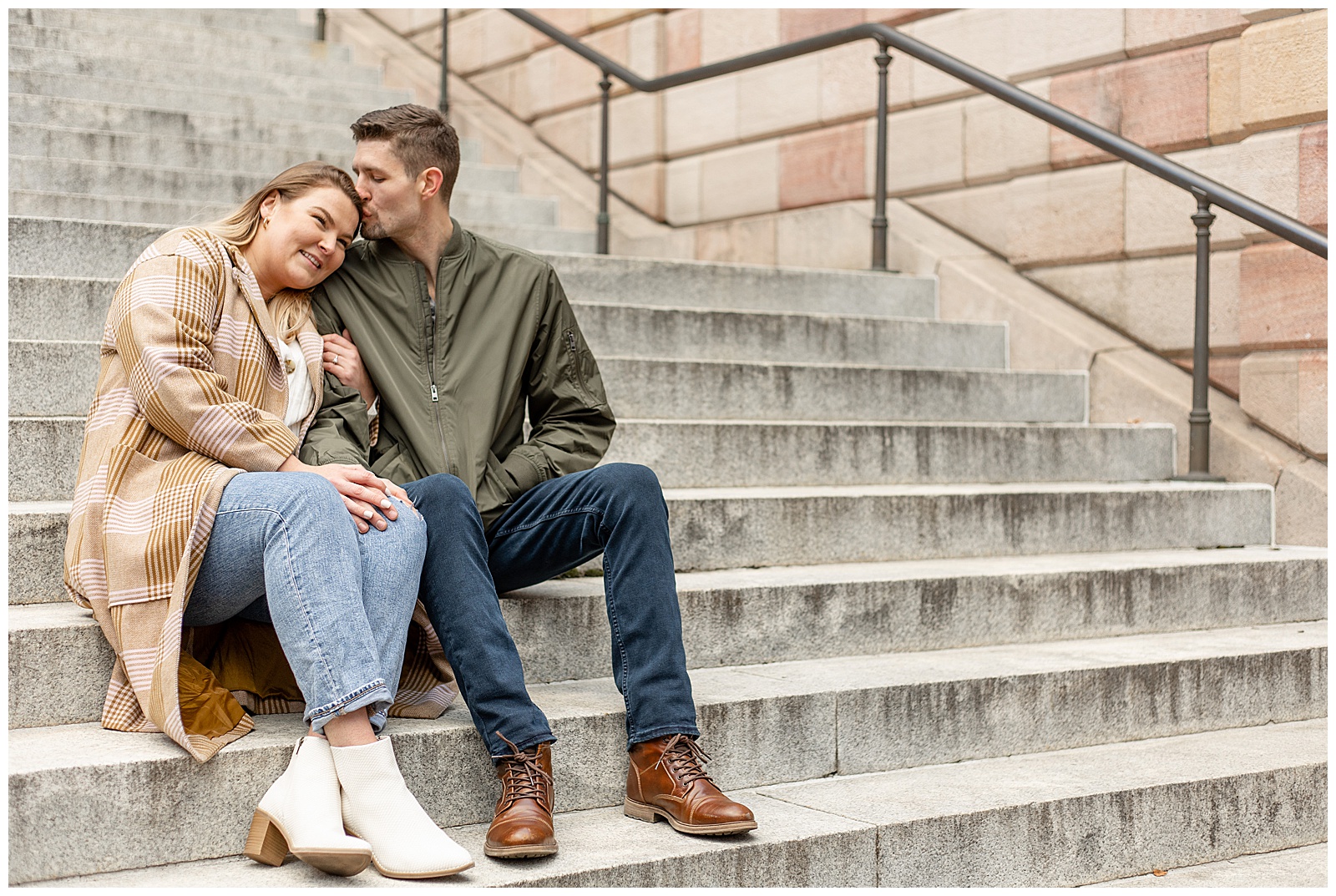 engaged couple sitting on county courthouse steps in downtown lancaster as guy kisses the top of girl's head