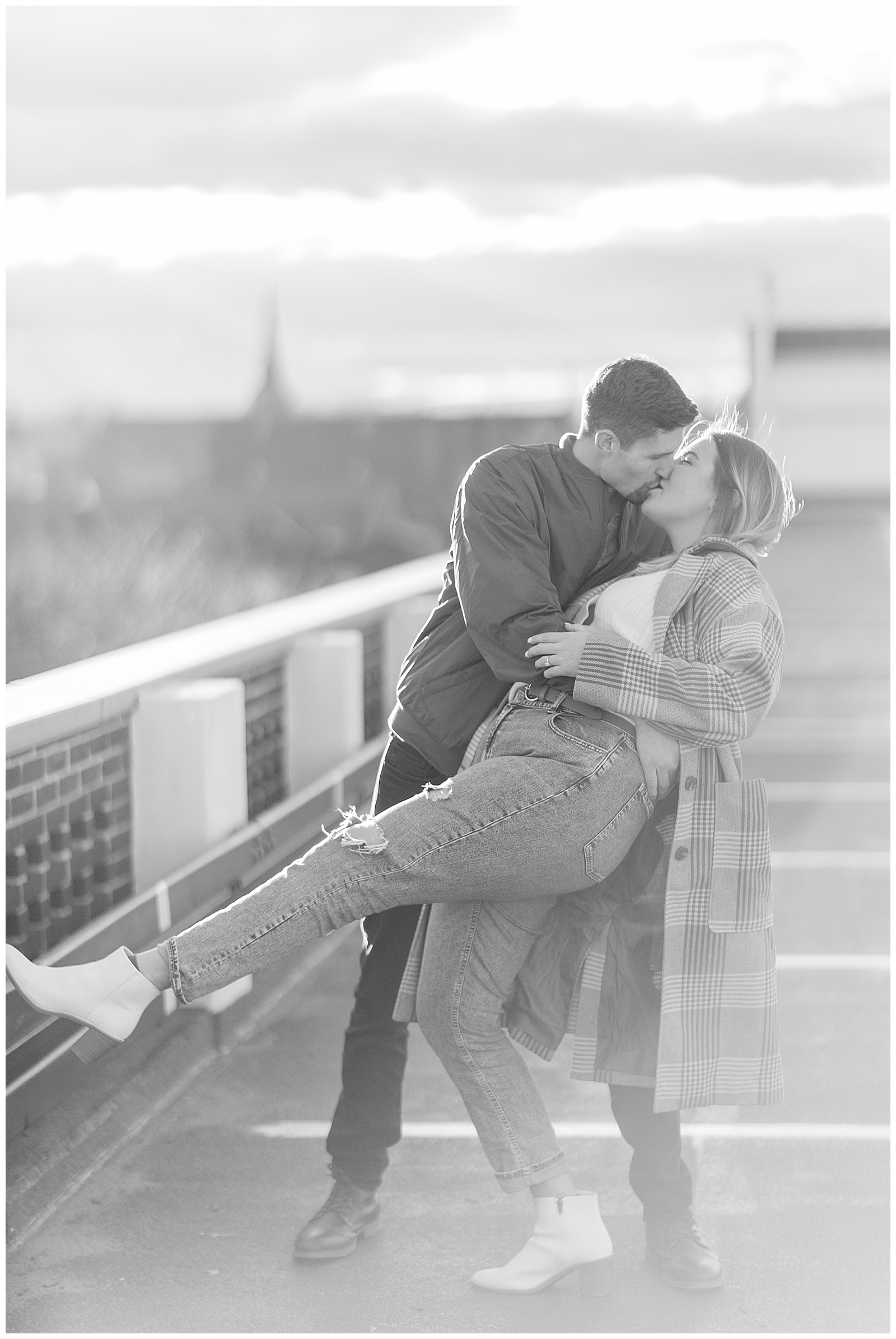 black and white photo of engaged couple kissing as guy dips girl back on top level of parking garage in lancaster pennsylvania