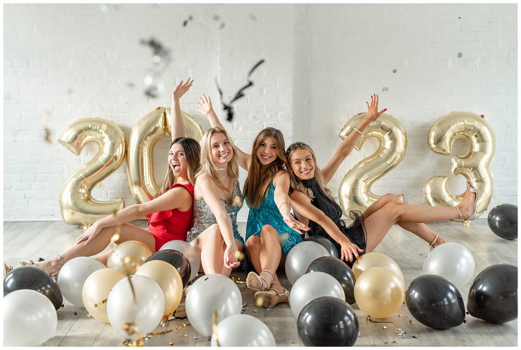 four senior spokesmodel girls in colorful dresses seated and surrounded by metallic colored balloons and confetti at the white room in lancaster pennsylvania