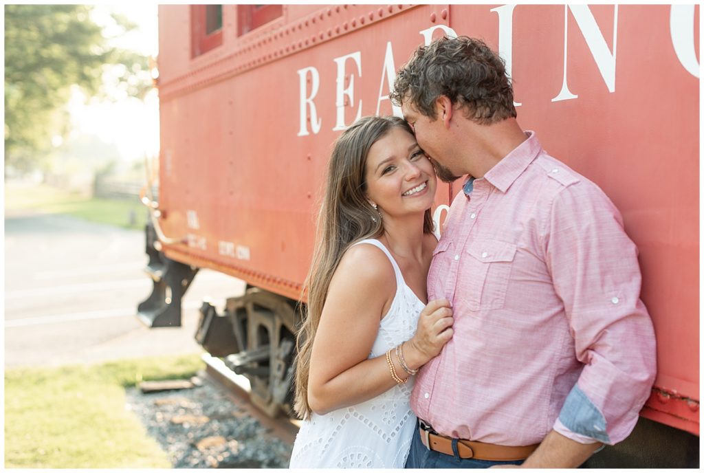 girl smiling at camera as guy kisses her left cheek and he leans against reading railroad train car in downtown lititz pennsylvania