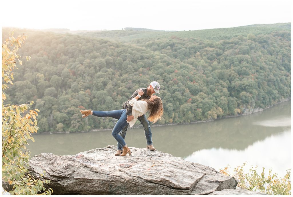 guy dipping back his girl as they kiss and she kicks out her right leg atop large rock at pinnacle overlook in holtwood pennsylvania