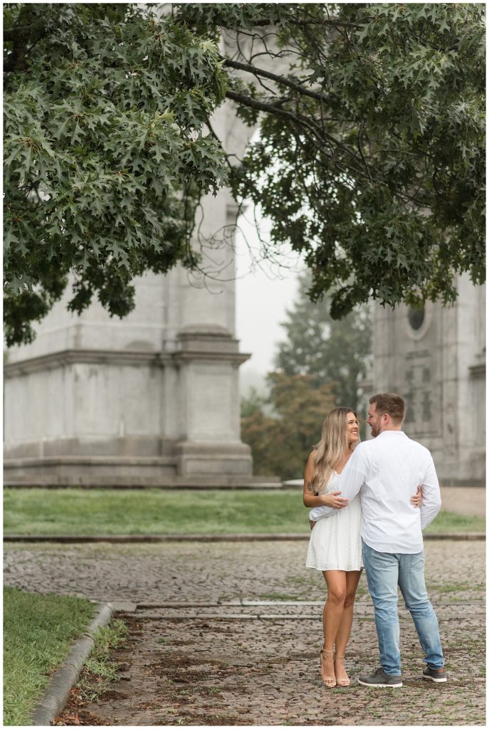 couple hugging with guy's back to camera and girl looking up at him in front of large monument at national memorial arch in valley forge pennsylvania