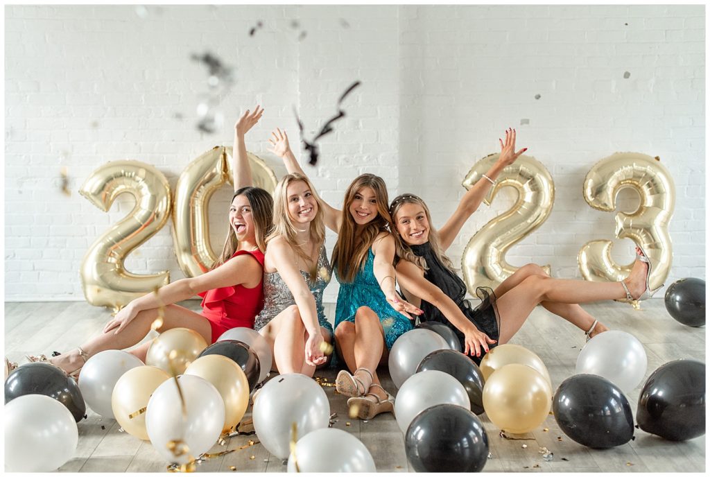 four senior girl spokesmodels with arms extended in excitement surrounded by silver, gold, and black balloons at the white room