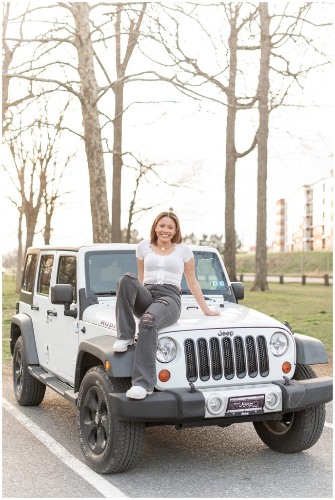 senior girl sitting on hood of her white jeep wrangler on sunny evening at lititz springs park in lancaster pennsylvania