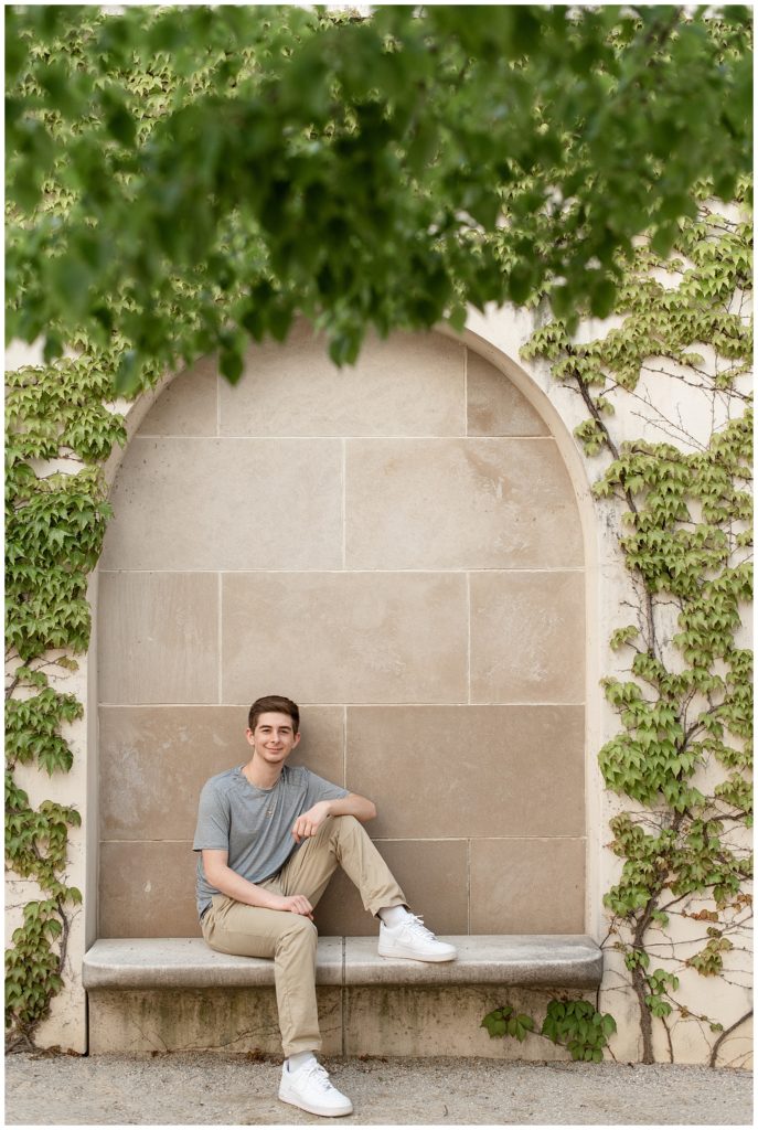 senior guy sitting on concrete bench inside concrete ivy-covered archway at longwood gardens in kennett square