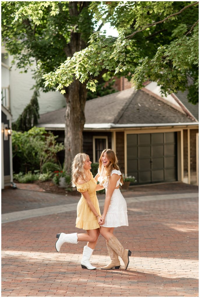 two senior girls facing each other and holding hands wearing short dress on sunny evening at old trinity place in lancaster pennsylvania