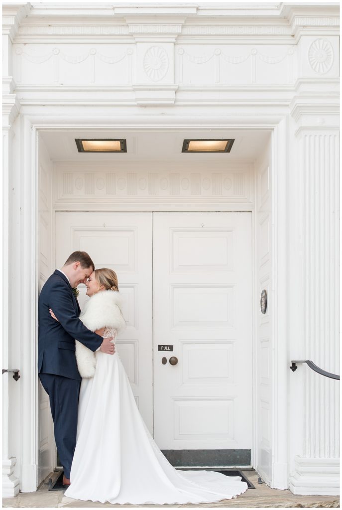 bride and groom hugging on cold winter day by large white doors in downtown lititz pennsylvania near the lititz springs inn and spa