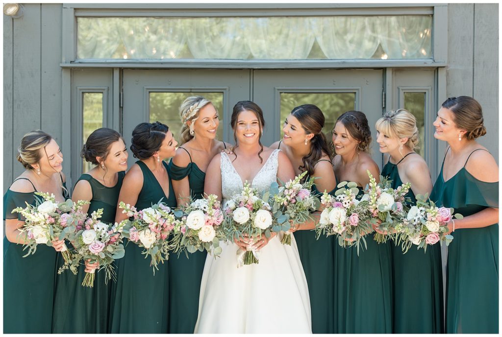 bride surrounded by her six bridesmaids all wearing dark green gowns and holding bouquets at this manor at mountain view wedding