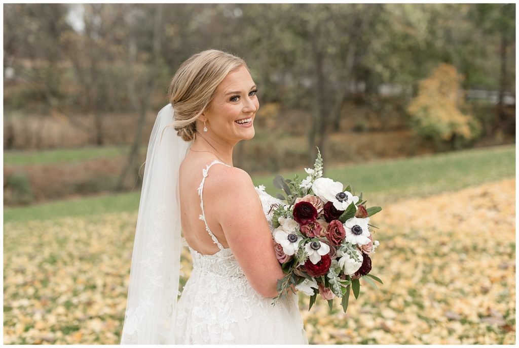 bride looking over her right shoulder with her back to the camera hold maroon and white bouquet at historic ashland
