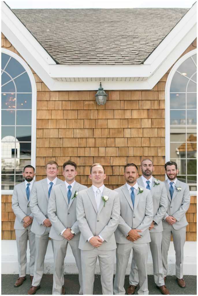 groom standing with his six grooms men forming a "v" behind him by wooden building in long island, new york