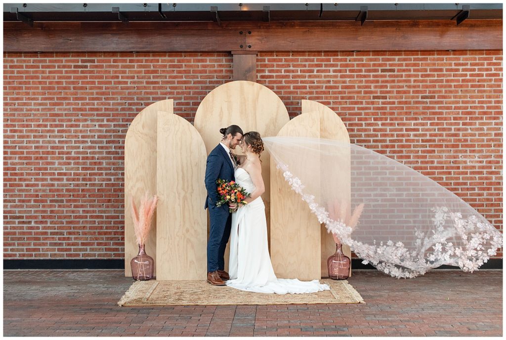 bride and groom standing by modern geometric wood backdrop by red brick wall at ironspire complex