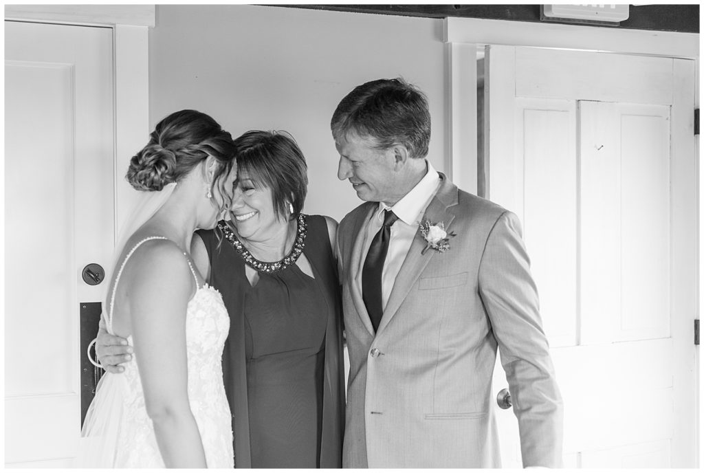 black and white photo of bride with her mom and dad in bridal suite during first look moment at lakefield weddings