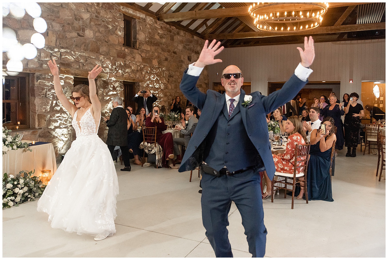 bride and her dad wearing sunglasses with hands in the air during their fun father-daughter dance inside barn reception at elizabeth furnace