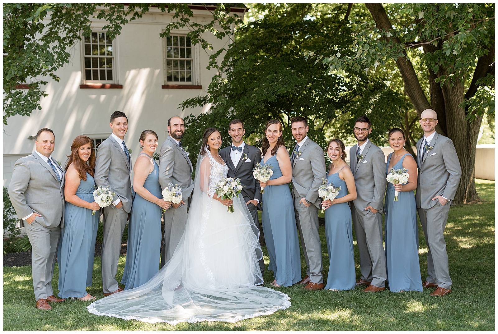 bride and groom with their bridal party outside white building at normany farm in blue bell pennsylvania