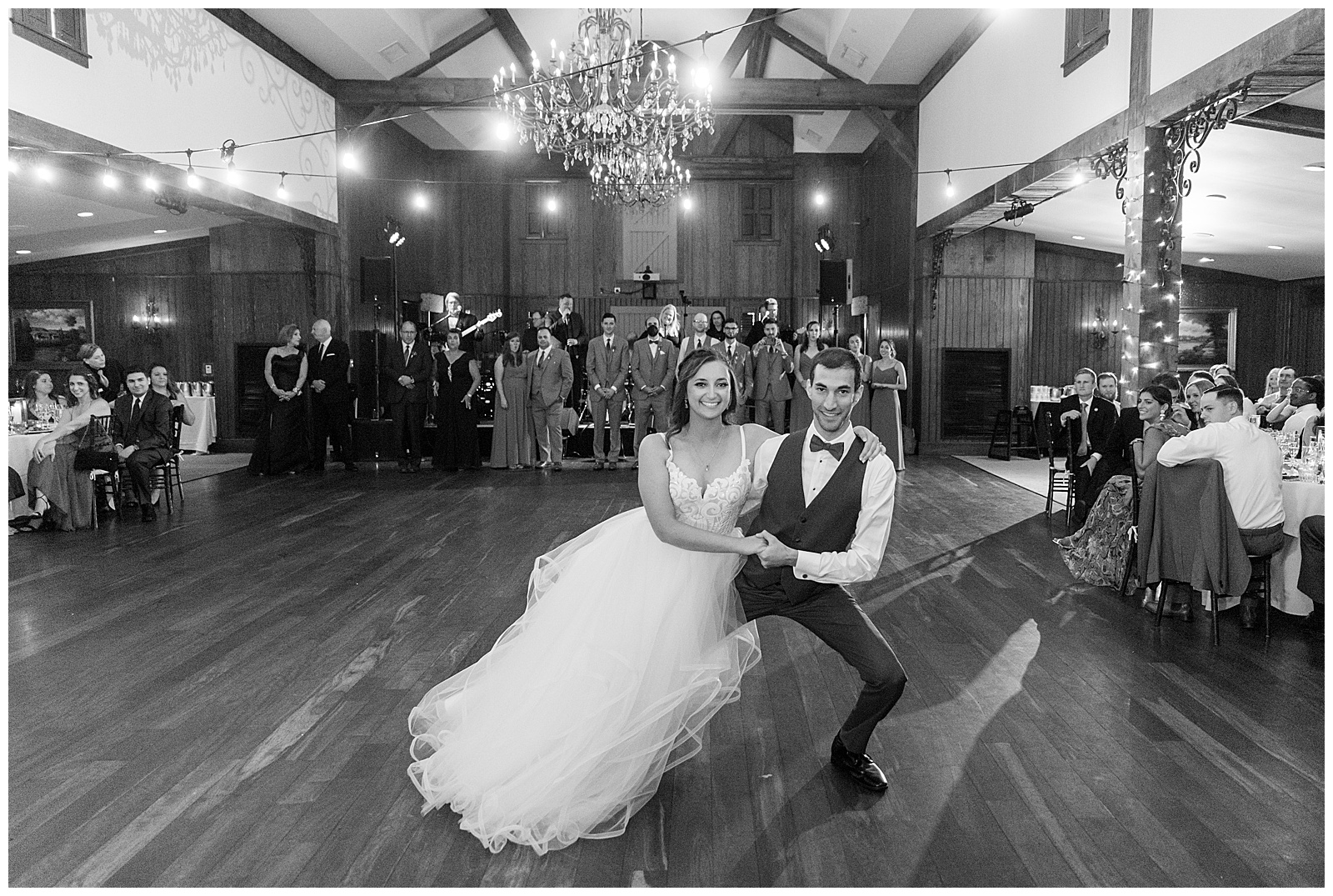 black and white photo of bride and groom sitting on chairs in center of dance floor with guests around them at normandy farm
