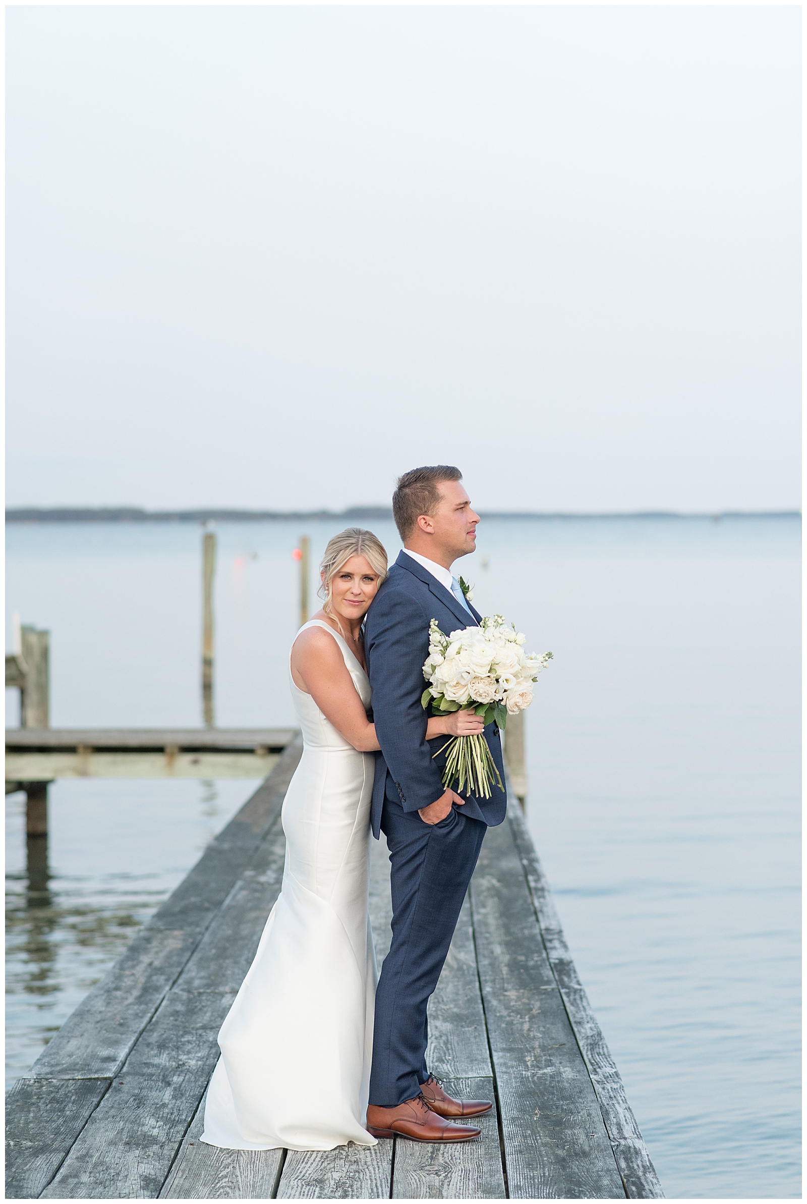 bride hugging her groom from behind on dock with ocean behind them as she smiles at camera at tilghman island