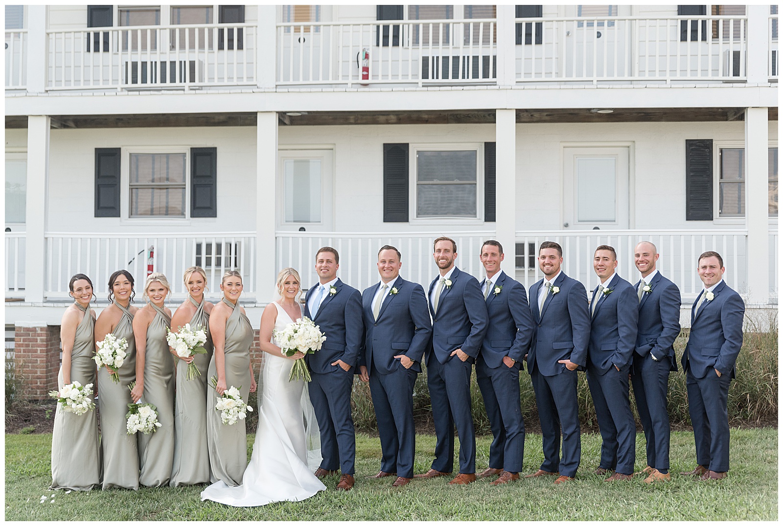 bride and groom with their bridal party in front of large white house with black shutters on tilghman island in maryland