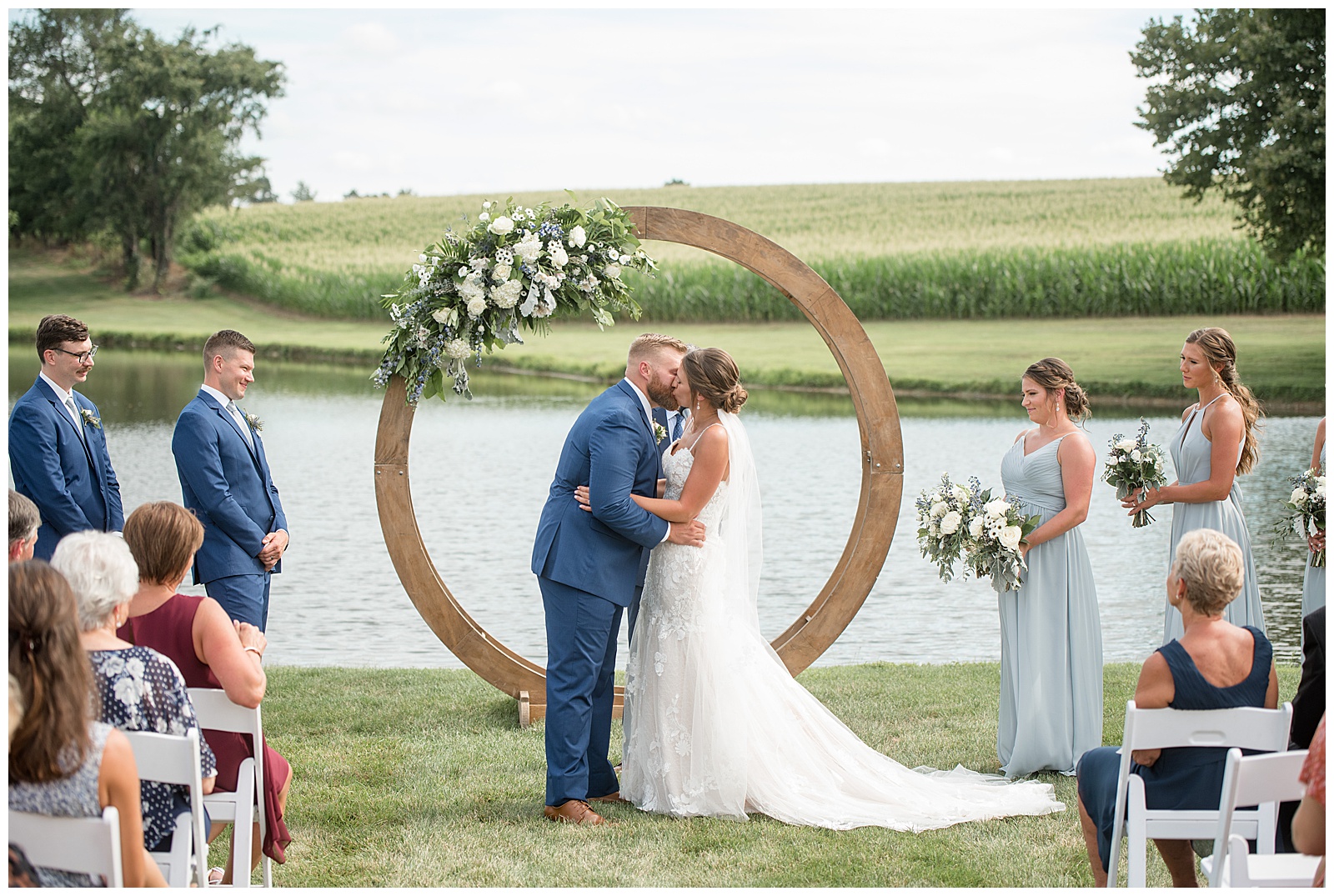bride and groom kissing during outdoor wedding ceremony by circular wooden and floral display by pond at lakefield weddings
