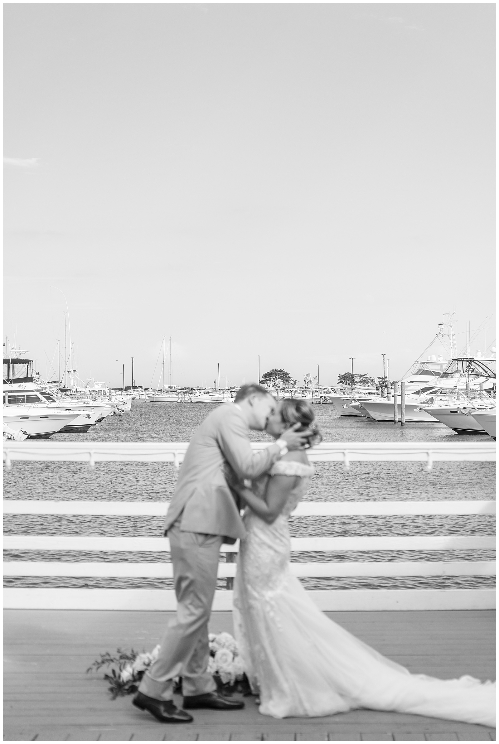 black and white photo of couple kissing by bay filled with boats in long island new york