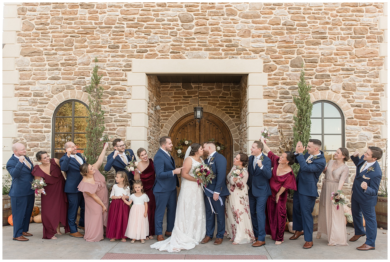 couple kissing surrounded by their cheering bridal party by stone building at folino estate winery in berks county
