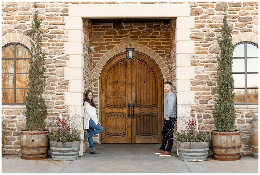 engaged couple standing in large doorway and leaning on opposite sides of stone door frame at winery in berks county