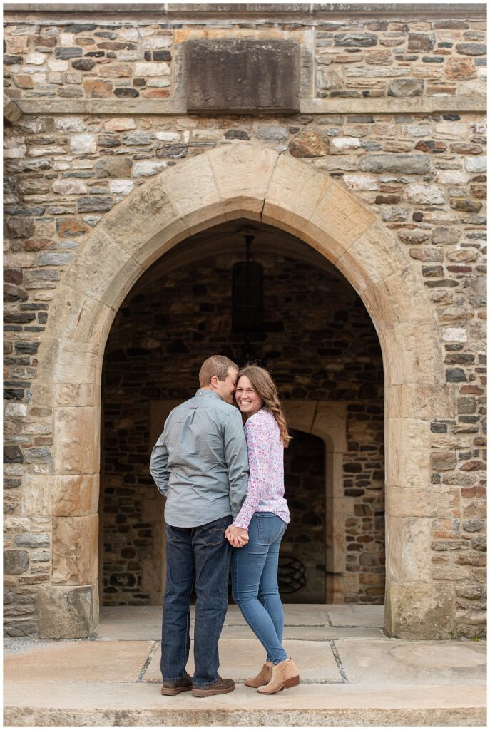 couple standing in beautiful stone archway with girl smiling at camera and guy's back to camera at ridley creek park
