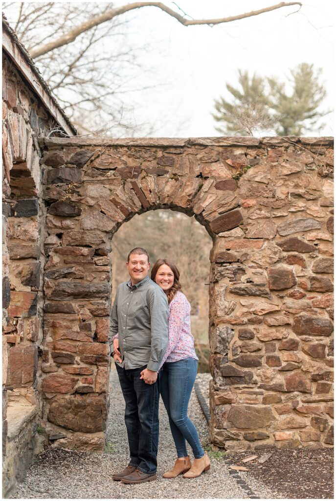 girl standing behind guy in stone archway as they both smile at camera on winter day in montgomery county pennsylvania