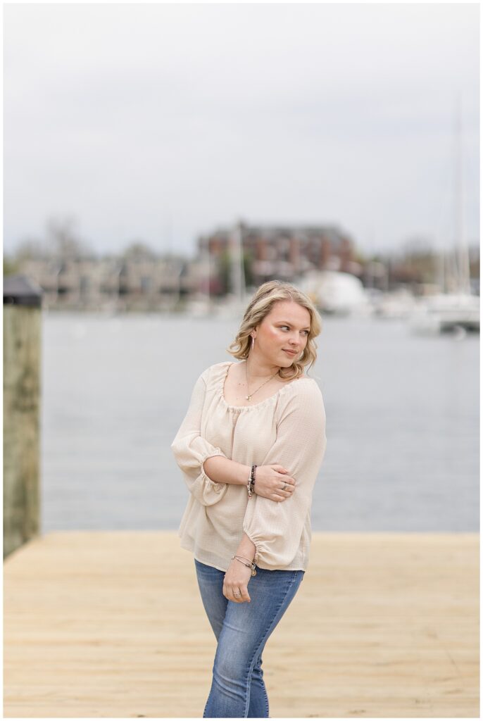 college senior girl standing on dock looking back over her left shoulder with her right hand on her left elbow in annapolis