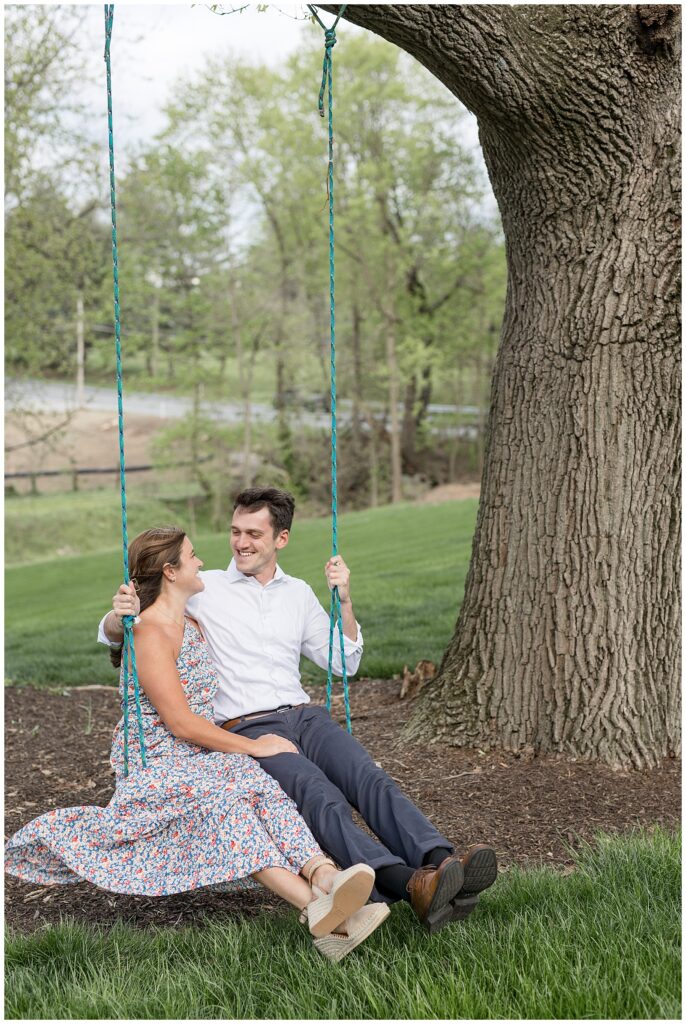 girl wearing floral dress sits on swing with her guy who's wearing white shirt and navy blue pants on overcast evening at historic ashland