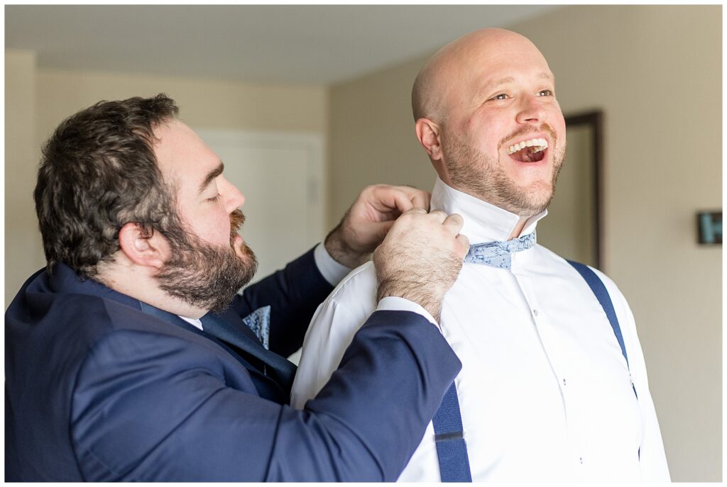 groom smiling big as his best man adjusts his blue suspender at rivercrest golf club
