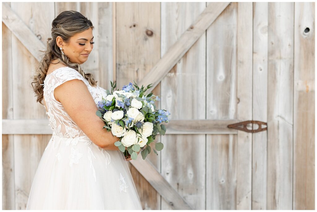 bride looking down at blue and white bouquet by lovely barn door at rivercrest golf club in montgomery county