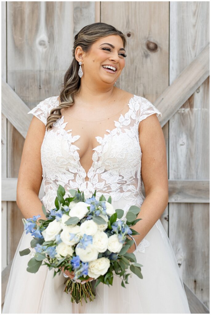 bride smiling big as she looks left holding bouquet and standing by wooden door on wedding day in pennsylvania