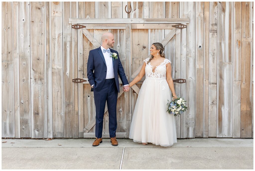bride and groom hold hands and look at each other in front of large wooden doors on wedding day in montgomery county pennsylvania